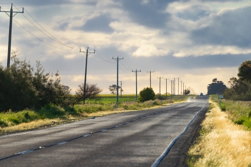 A long straight country road under an overcast sky with a row of power poles along side - Australian Stock Image
