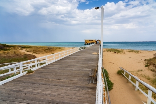 A long wooden jetty leading out over a beach to a boat shed - Australian Stock Image