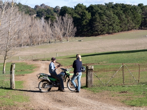 A male farmer on a motorbike in discussion with a female farmhand