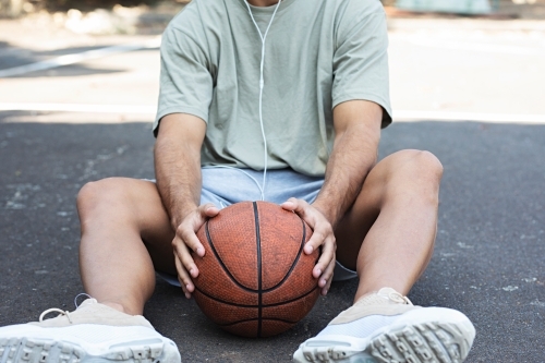 A male in his twenties holding a basketball / taking a break on an outdoor basketball court - Australian Stock Image