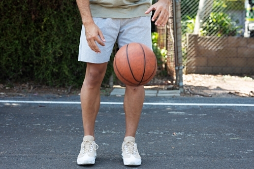 A male in his twenties with a basketball / taking a break on an outdoor basketball court - Australian Stock Image