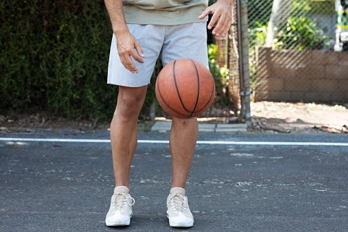 A male in his twenties with a basketball / taking a break on an outdoor basketball court