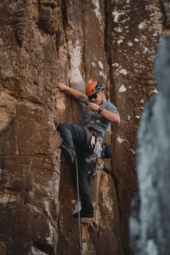 A male rock climber placing 'trad' gear into a cliff for a climbing route at Diamond Beach. - Australian Stock Image