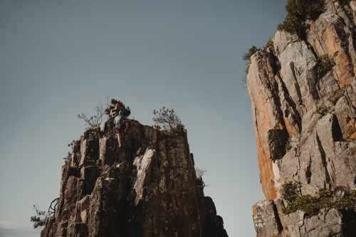 A male rock climber summits a climbing route at Diamond Beach. - Australian Stock Image