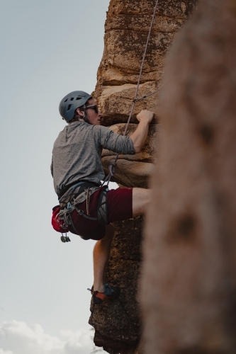 A male rock climber tackling a climbing route at Diamond Beach. - Australian Stock Image