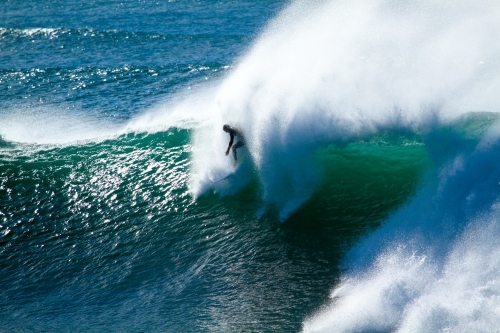A male surfer in his late twenties surfing a large powerful wave at Sandon Point, NSW
