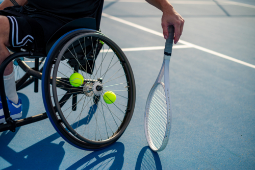 A male wheelchair tennis player is ready, holding a racquet near tennis balls on the court. - Australian Stock Image