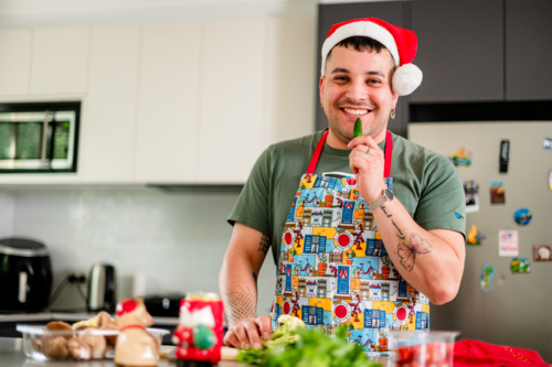 A man in a Santa hat smiles while cooking with fresh produce in a vibrant kitchen - Australian Stock Image