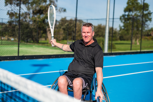 A man in a wheelchair gets ready to smash on a tennis sesh - Australian Stock Image