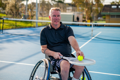 A man in a wheelchair holds a tennis ball on a blue court in Australia - Australian Stock Image
