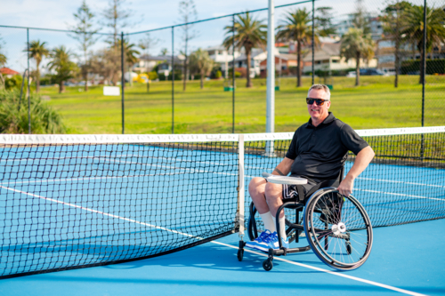 A man in a wheelchair is playing tennis on a hard court - Australian Stock Image