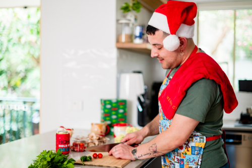 A man in an apron cutting tomatoes in kitchen - Australian Stock Image
