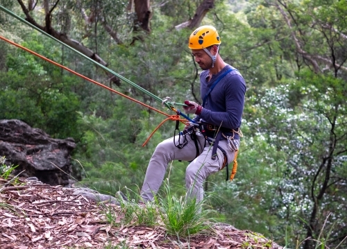 a man in full safety gear, abseiling down a cliff