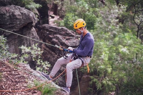 a man in full safety gear, abseiling down a cliff
