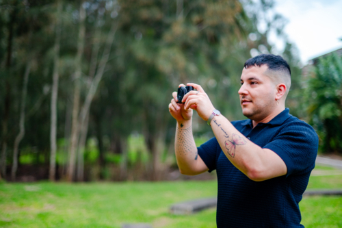 A man in his 30s is taking pictures in a park, enjoying outdoor photography and leisure time - Australian Stock Image