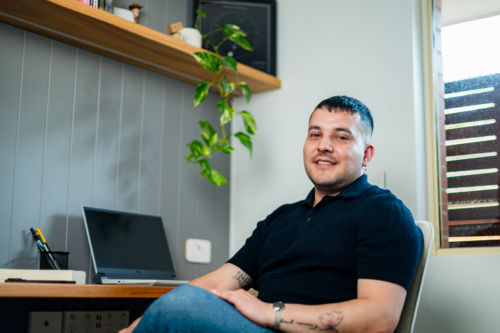 A man in his 30s sitting at a home desk with a computer - Australian Stock Image