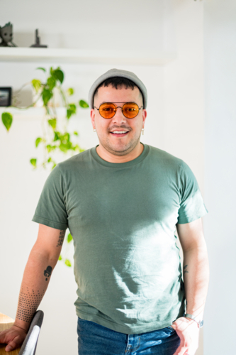 A man in his 30s smiles warmly, wearing a stylish outfit and glasses in a bright, airy room - Australian Stock Image
