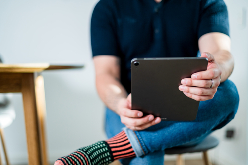 A man in his thirties sits at home, engaging with content on his tablet - Australian Stock Image