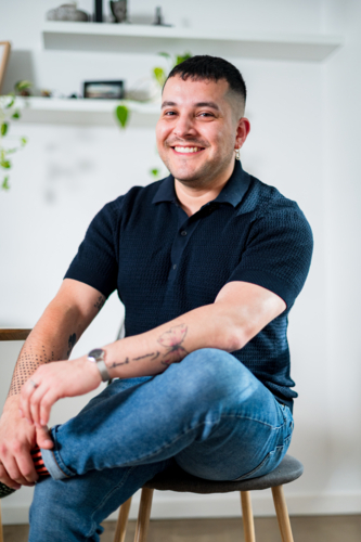 A man in his thirties smiles confidently while sitting comfortably, showcasing his relaxed style. - Australian Stock Image
