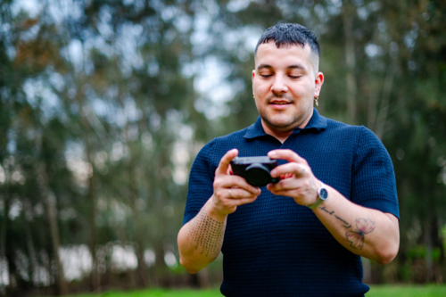A man in his thirties stands in a park, capturing moments with a digital camera on a overcast day - Australian Stock Image