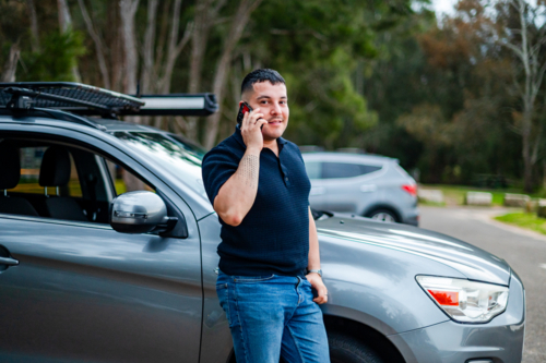 A man in his thirties stands outside his car, smiling as he chats on his phone. - Australian Stock Image