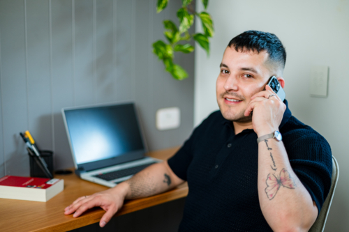 A man in his thirties talking on the phone in a cosy home office - Australian Stock Image