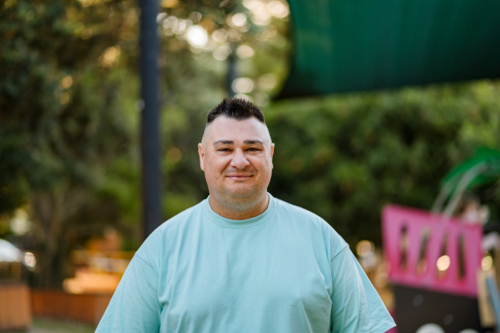A man is smiling while standing in a park with playground areas and trees around him - Australian Stock Image