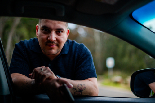 A man leans on a car window form outside vehicle in a park setting - Australian Stock Image