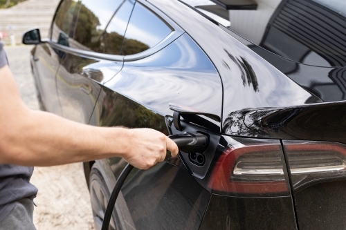 A man plugging in an electric Ev vehicle car to a home charger station plug - Australian Stock Image