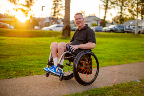 A man rides his wheelchair along a footpath while the sun sets in the background - Australian Stock Image