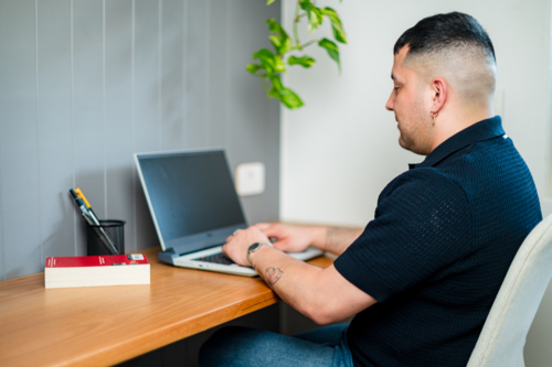 A man sits at his desk with a laptop, focused on his work in a cosy home office. - Australian Stock Image