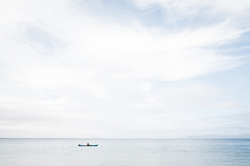 A man using a blue Kayak in the Ocean on a still but cloudy day - Australian Stock Image