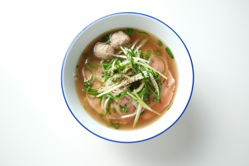 A meatball noodle soup topped with green onions surrounded by spices on the surface. - Australian Stock Image
