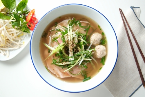 A meatball noodle soup topped with green onions surrounded by spices on the surface. - Australian Stock Image