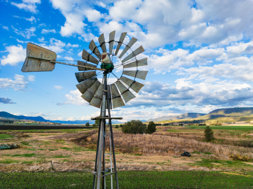 A metal windmill above a field and hilly area in south east Queensland - Australian Stock Image