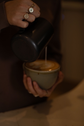 A milk poured from a black pitcher into a cup of coffee - Australian Stock Image