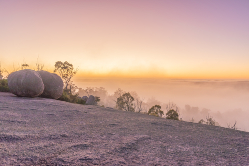 A misty sunrise under pink skies on a granite monolith - Australian Stock Image