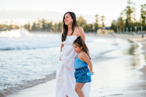 A mother and daughter enjoy time together on the beach as waves crash nearby - Australian Stock Image