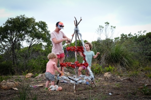 A mother and two toddlers celebrating Christmas decorating a rustic Christmas tree - Australian Stock Image
