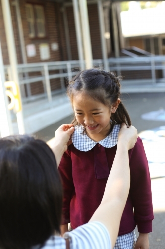 A mother fixing her daughters school collar at school - Australian Stock Image