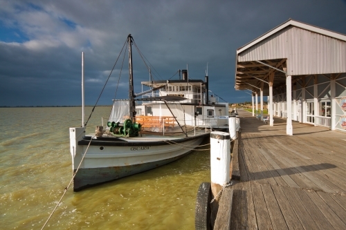 A paddle steamer tied to a wharf under a dark morning sky - Australian Stock Image