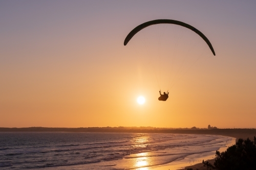 A paraglider in the sky at sunset over the beach - Australian Stock Image
