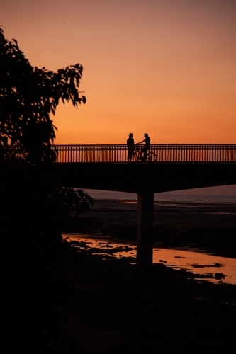 A pedestrian and cyclist on a bridge at sunset - Australian Stock Image