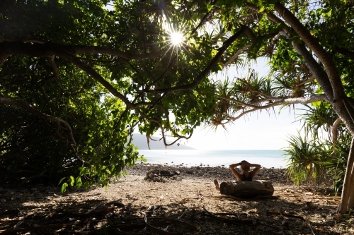 A person relaxing in the shade of tropical trees on a bright, sunny day at a remote beach