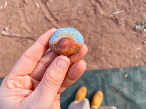 A person’s hand holding a small, round, colourful painted stone. - Australian Stock Image