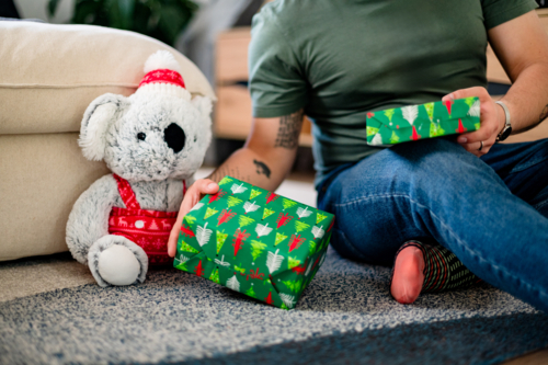 A person sits on the floor with colourful gifts beside a festive koala decoration - Australian Stock Image