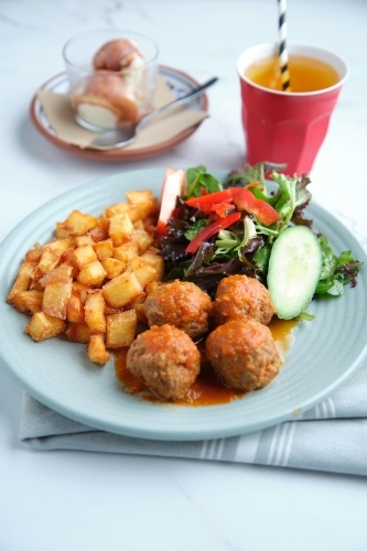 A plate of diced potatoes, salad and meat balls with dessert and drinks - Australian Stock Image