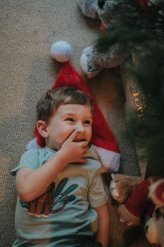 A playful child with a Santa hat laughs while lying on the floor - Australian Stock Image