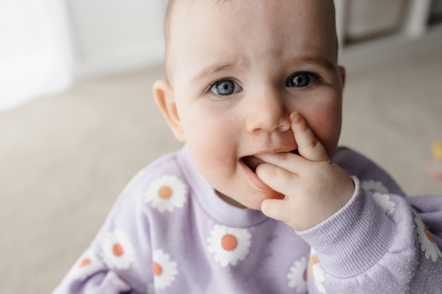 A portrait of a one year old girl looking at the camera with her hand in her mouth