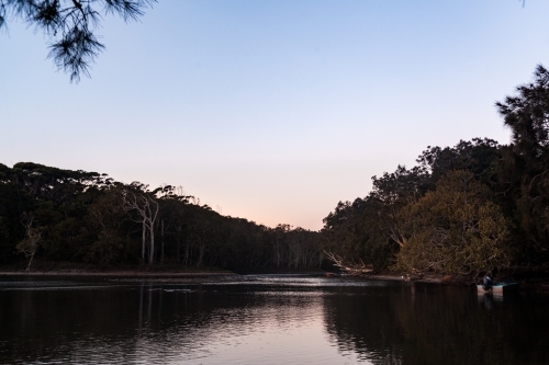 A quiet lake at dusk surround by bush and tree with small boats docked on the right. - Australian Stock Image